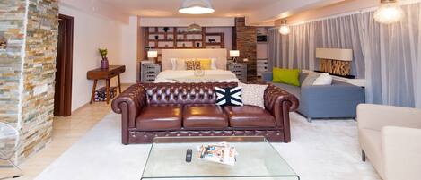 A modern living room with a leather sofa, a glass coffee table, and a bed with a headboard.