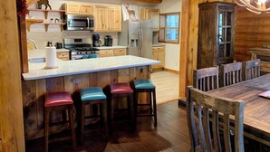 L’intérieur d’un chalet rustique présente une cuisine avec des meubles en bois, un comptoir en marbre et un îlot central doté de tabourets.