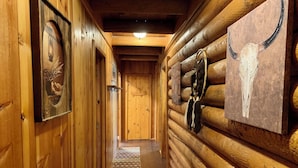 Un couloir dans une cabane en rondins de bois, avec des tableaux encadrés et un crâne de vache en guise de décoration.