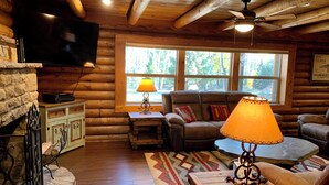 L’intérieur d’un chalet confortable, avec des murs en rondins de bois, une cheminée en pierre, des meubles en bois et une grande fenêtre donnant sur le paysage extérieur.