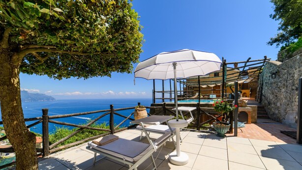 A terrace with a view of the sea, outdoor seating, and a pergola.