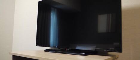 A flat-screen TV mounted on a wall above a wooden entertainment unit with a DVD player and a remote control.