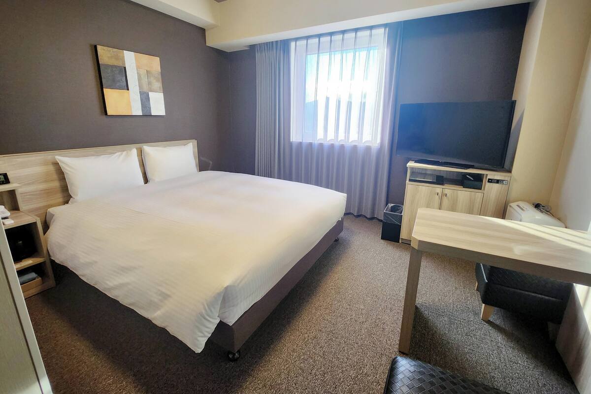 A hotel room with a large bed, a television, a desk, and a window with curtains.