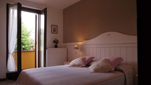 A bedroom with a bed, pillows, a nightstand, a wall-mounted lamp, and a window with curtains. - Affittacamere Marisa (Valeggio sul Mincio)