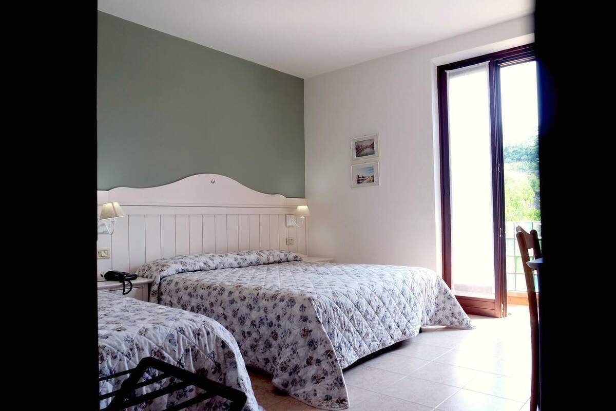 A bedroom with two beds, a window, and a door leading to a balcony.