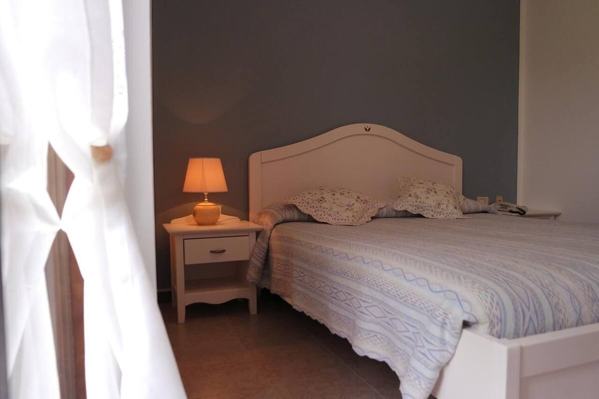 A bedroom with a bed, a nightstand with a lamp, and a bedside table.