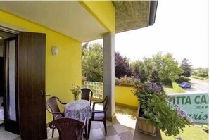 A yellow room with a table and chairs, a door, and a view of greenery and a sign outside. - Affittacamere Marisa (Valeggio sul Mincio)