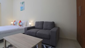 A hotel room with a bed, a gray sofa, a wooden coffee table, and a painting on the wall.