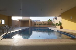 Una piscina interior con agua cristalina, rodeada de paredes color beige y un suelo de baldosas.