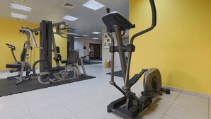 A gym with various exercise equipment, including a treadmill and weight machines, against a yellow wall.