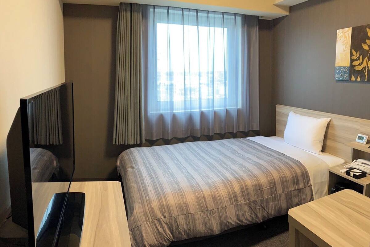 A hotel room with a large bed, a desk, a TV, and a window with curtains.