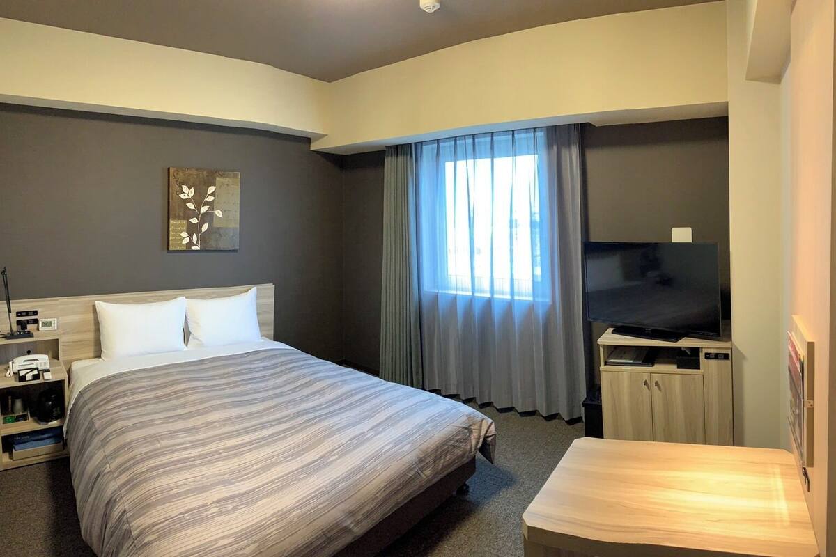 A hotel room with a bed, a desk, a TV, a coffee machine, and a painting on the wall.