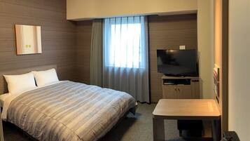 Une chambre d’hôtel avec un grand lit, une télévision, une petite table et une fenêtre avec des rideaux.