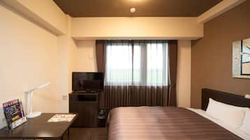 A hotel room with a bed, a desk with a TV, a small kitchenette, and a window with curtains.