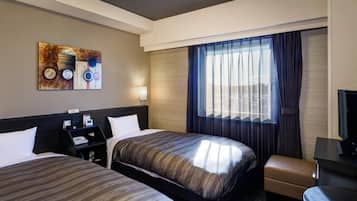 Habitación de hotel con dos camas, un escritorio con computadora, un televisor y una ventana con cortinas.