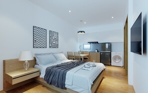 A modern bedroom with a bed, bedside table, and a small desk. There is a kitchen area with a refrigerator, washing machine, and a dining table with chairs.