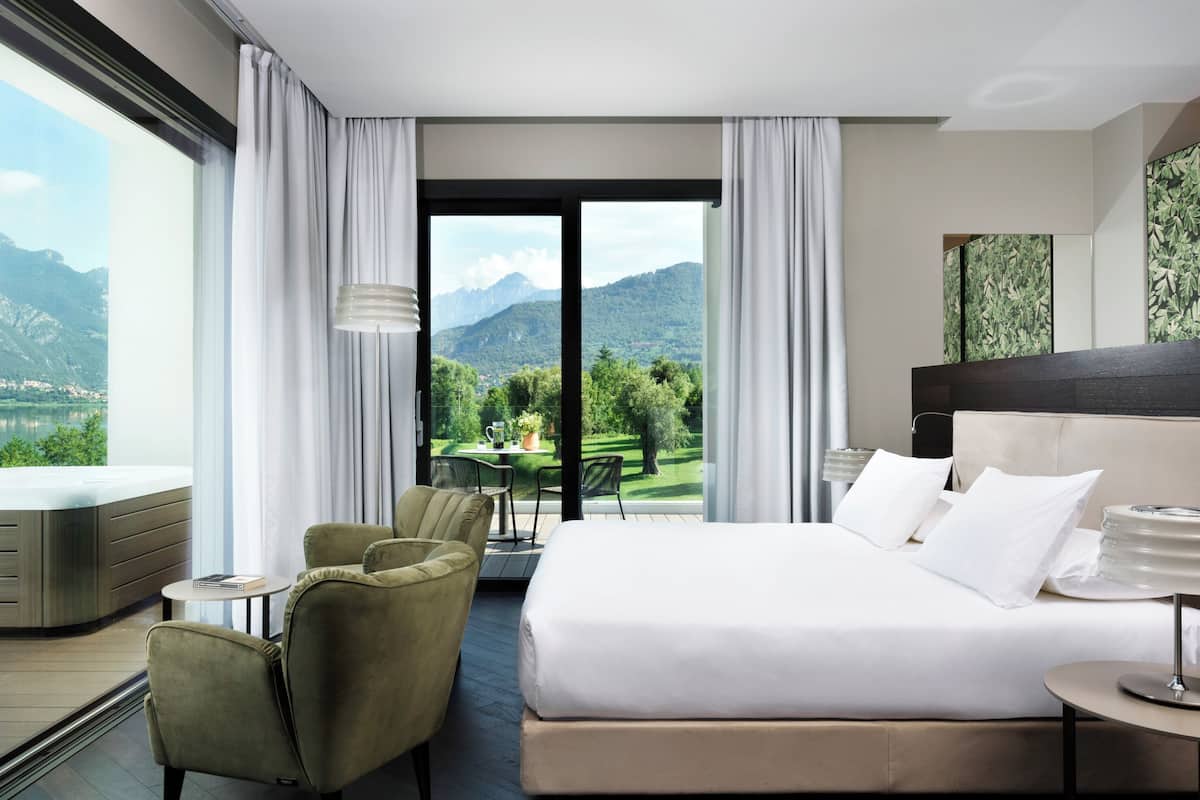 A hotel room with a bed, a seating area with chairs, a table, and a view of mountains.