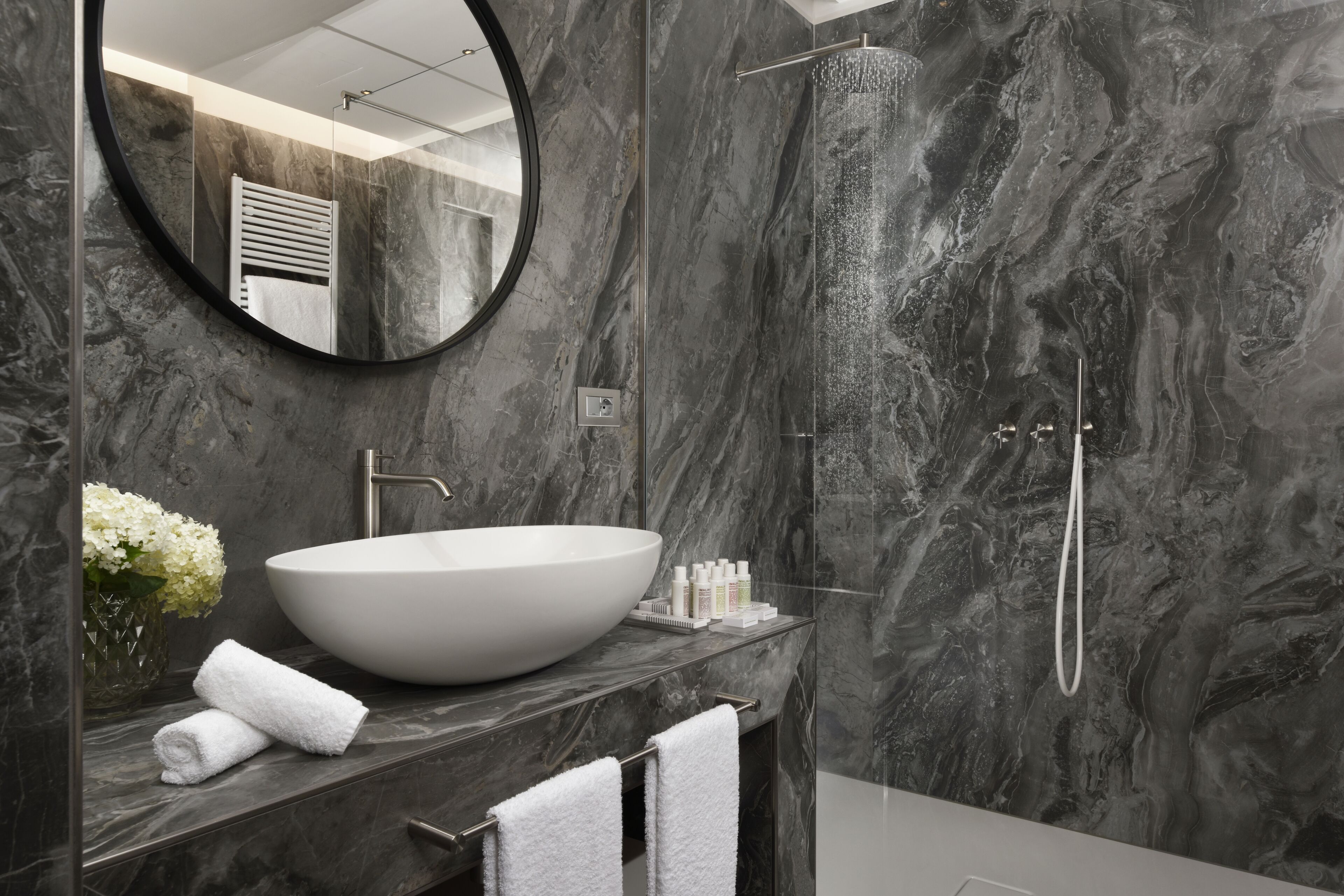 A modern bathroom with a large oval sink, a round mirror, and a shower area.