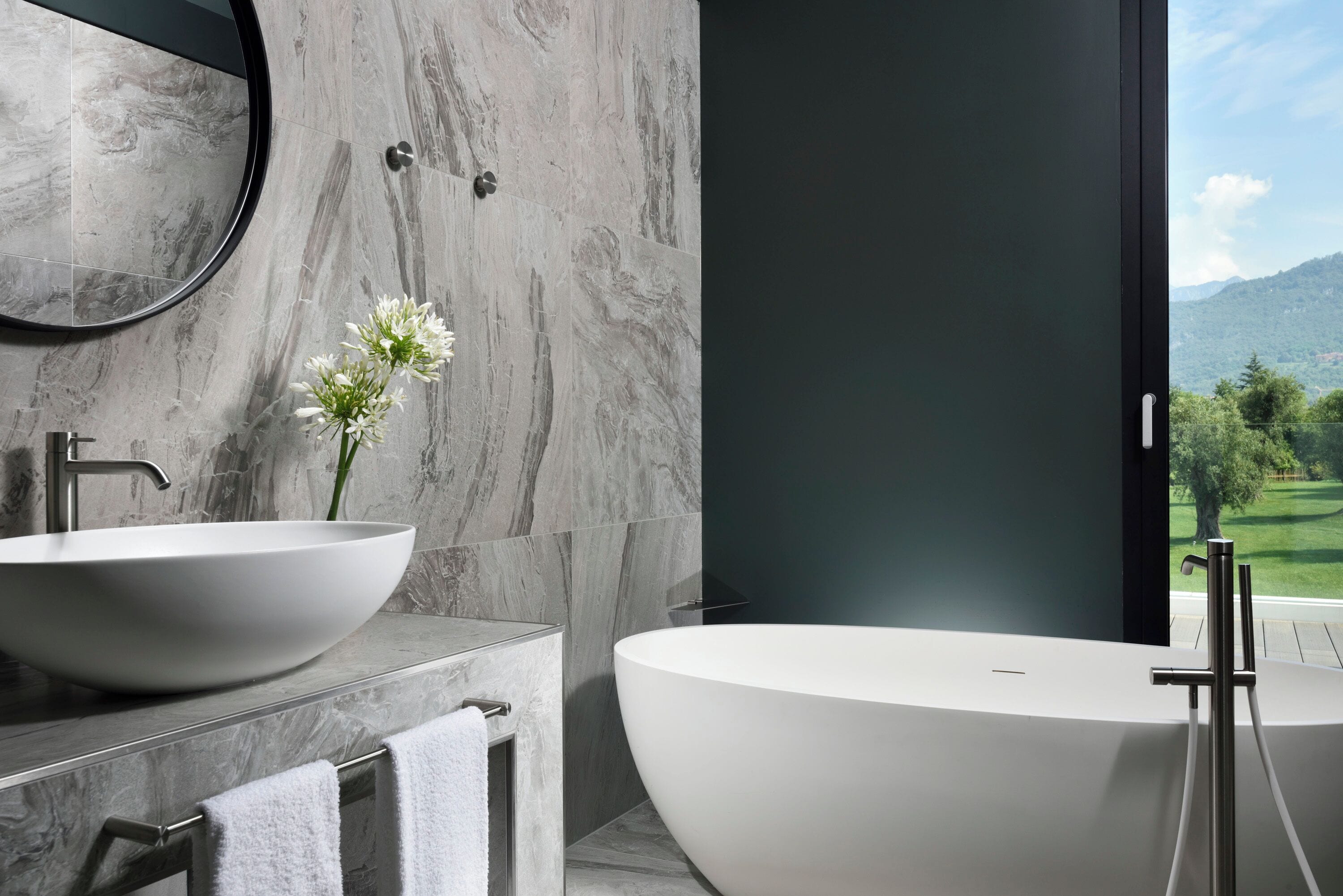 Une salle de bain moderne avec une grande baignoire ovale, un miroir rond et un lavabo blanc.