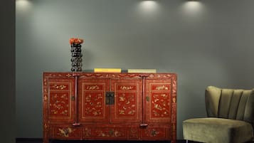 A traditional red cabinet with floral designs, a vase with flowers, and a chair.