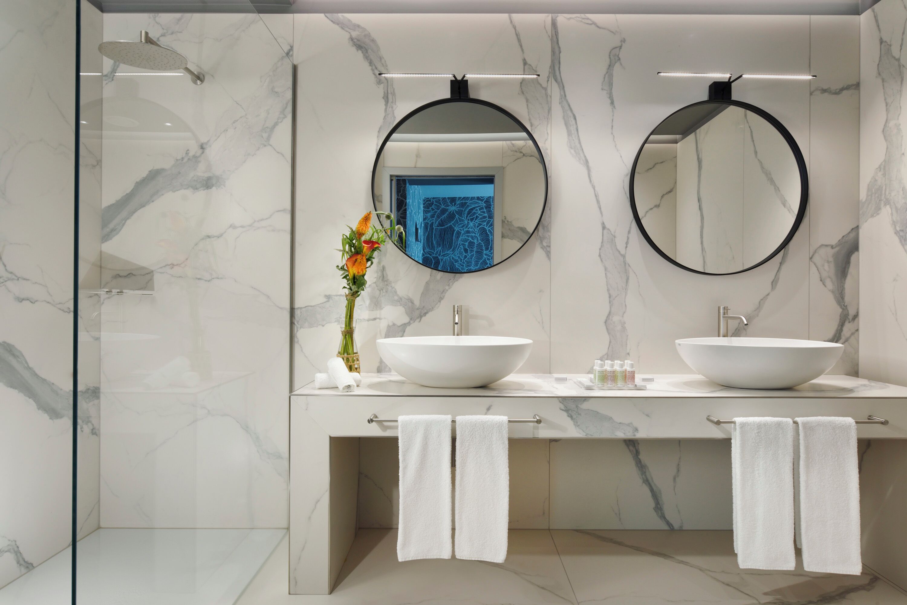A modern bathroom with two sinks, a large mirror, and a glass shower enclosure.