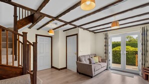 A spacious living room with a wooden staircase, a sofa, and a sliding glass door leading to a garden. - Conveniently located to explore all that Cornwall and Devon have to offer (SALTASH)