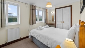A bedroom with a bed, a bedside lamp, a window with curtains, a radiator, and a door. - Conveniently located to explore all that Cornwall and Devon have to offer (SALTASH)