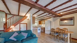 A living room with a blue sofa, wooden dining table, and chairs, a kitchen with appliances, and a staircase. - A spacious 2 bedroom property (SALTASH)