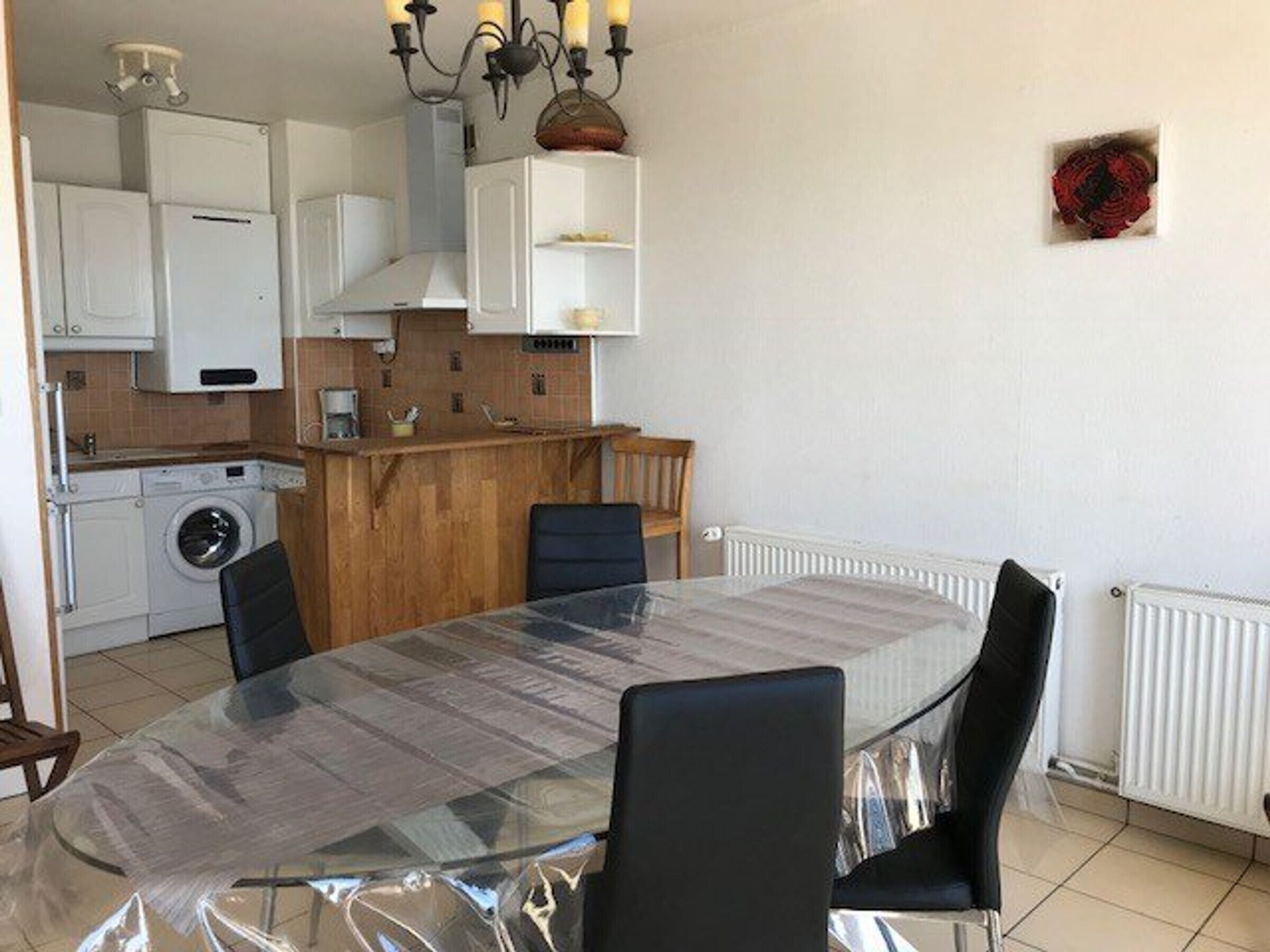 A compact kitchen with a dining area, including a washing machine, a wooden countertop, and a table with chairs.