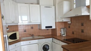 A compact kitchen with white cabinets, a built-in washing machine, a coffee maker, and a stove. - Duplex T3 for 6, beach nearby, private parking (Le Barcarès)