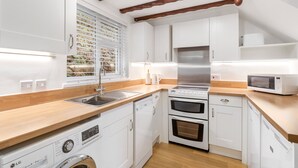 A compact kitchen with white cabinets, a wooden countertop, a stainless steel range, a microwave, and a washing machine. - A very spacious and versatile property suitable for couples, young families and those with an infant (SALTASH)