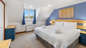 A bedroom with a large bed, a wooden headboard, a window with blue curtains, a blue nightstand, and a blue cabinet. - A very spacious and versatile property suitable for couples, young families and those with an infant (SALTASH)