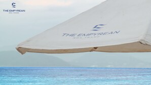 A person sitting on a beach chair under a large umbrella, holding a drink. - The Empyrean Nha Trang (Nha Trang)