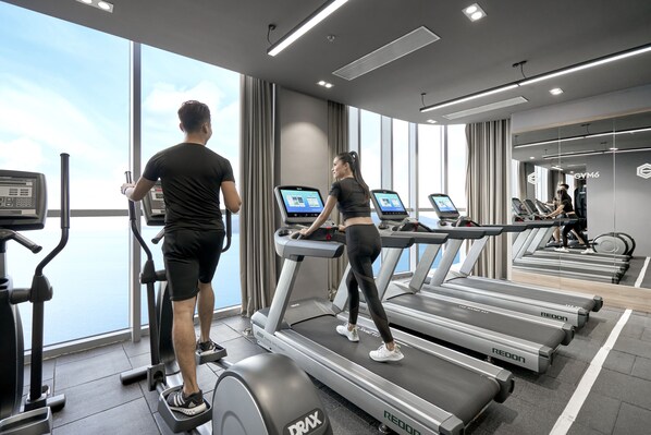 Un gimnasio moderno con cintas de correr, elípticas y un amplio ventanal con vistas al cielo.
