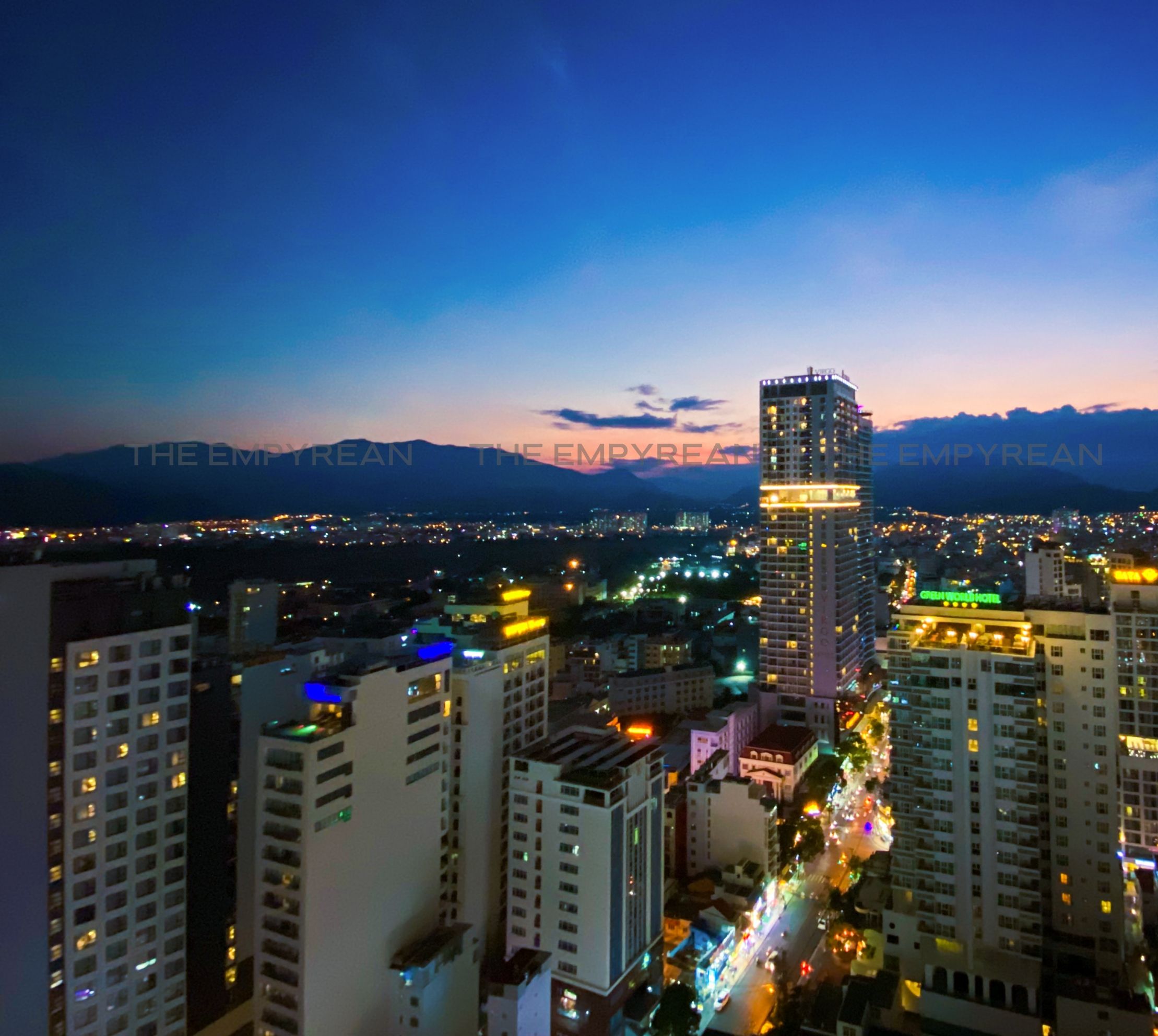 Un paisaje urbano al atardecer con edificios iluminados y un hotel destacado.