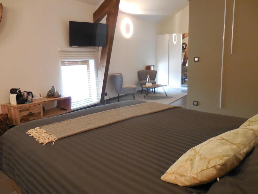 Une chambre à coucher avec un grand lit, un téléviseur fixé au mur, un bureau avec une chaise et une fenêtre avec des stores.