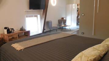 Une chambre à coucher avec un grand lit, un téléviseur fixé au mur, un bureau avec une chaise et une fenêtre avec des stores.