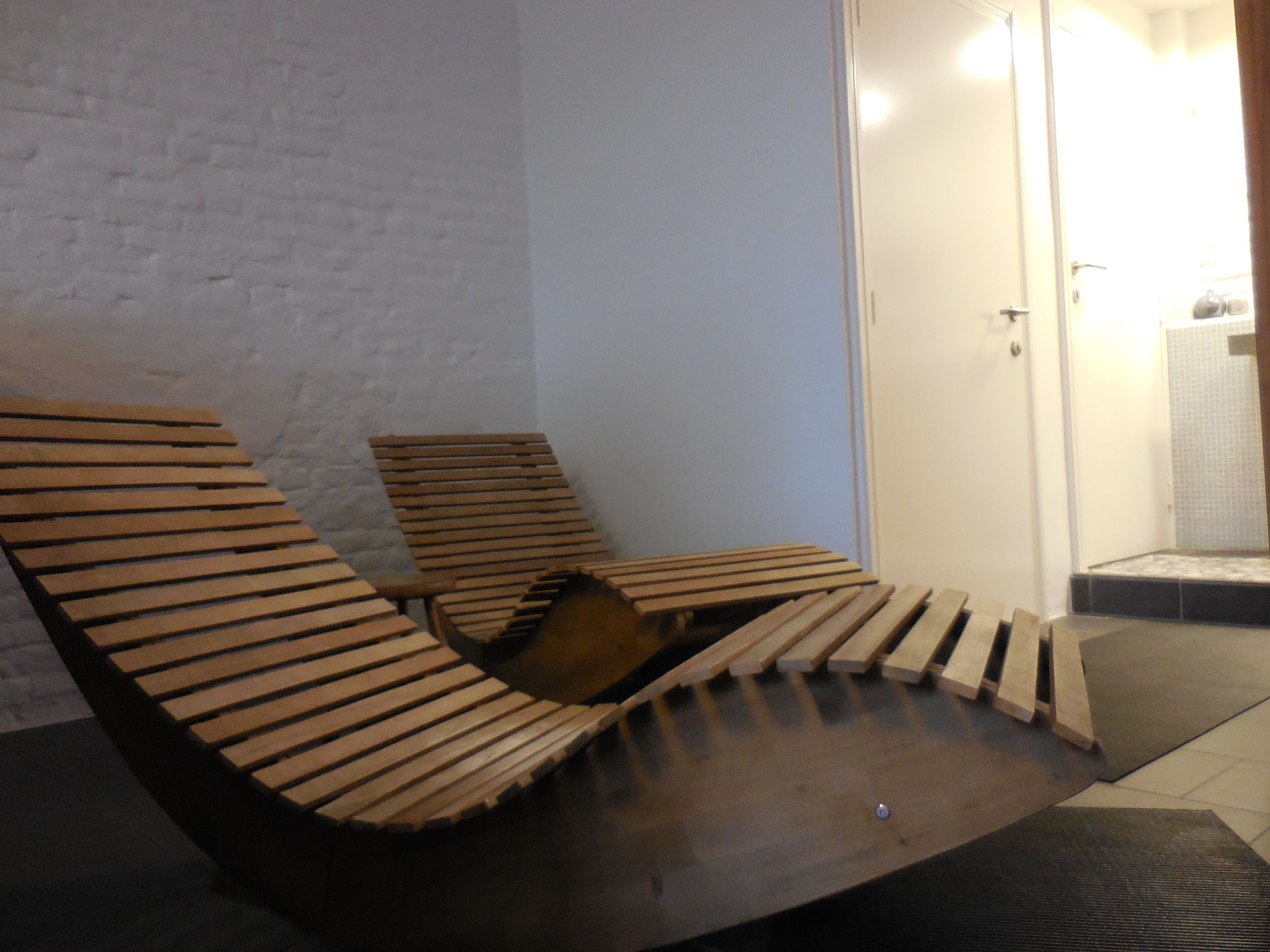 Une pièce avec un mur en briques blanches, un banc en bois et une porte donnant sur une salle de bain.