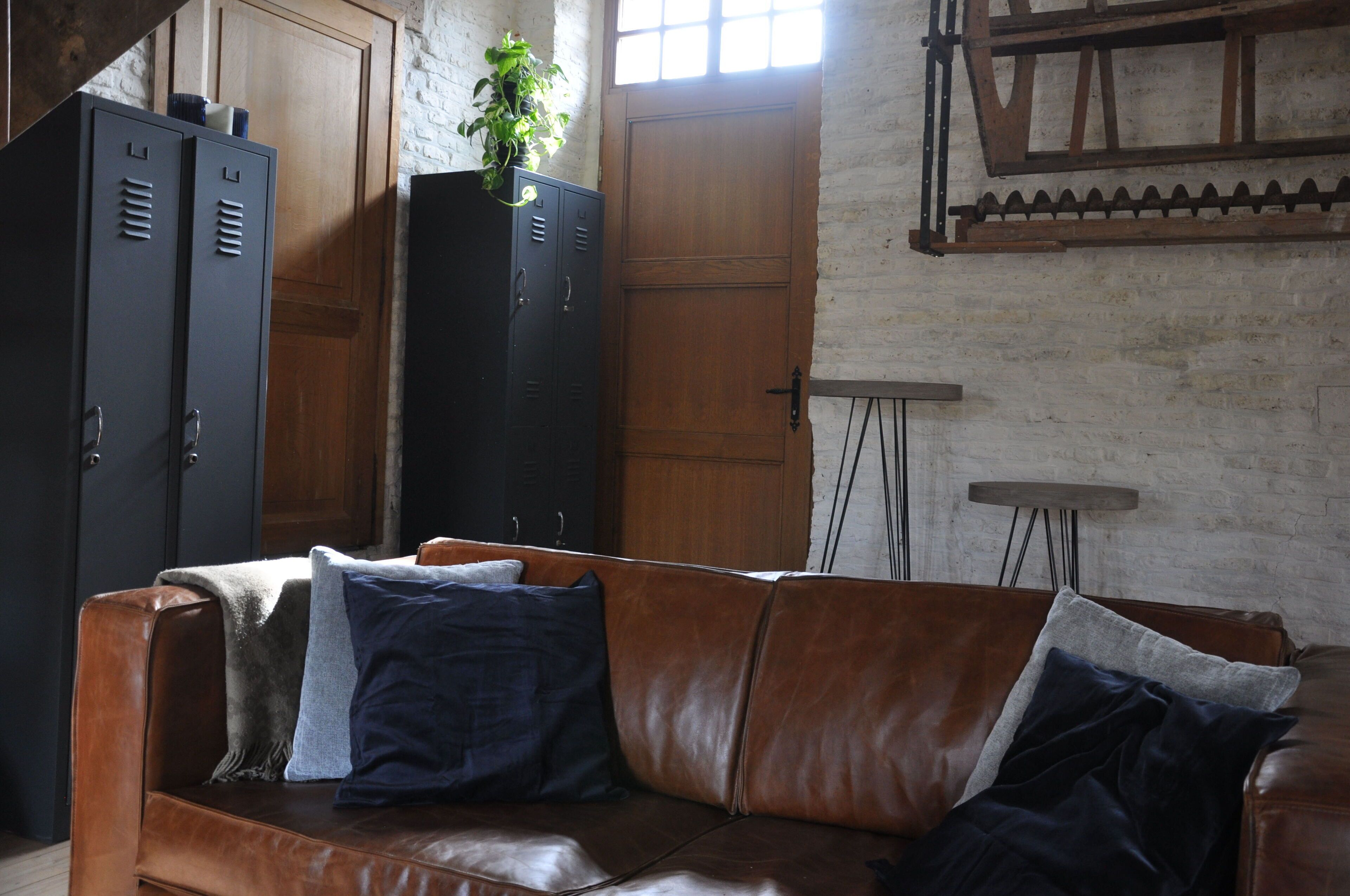 A room with a leather couch, wooden cabinets, and a brick wall.