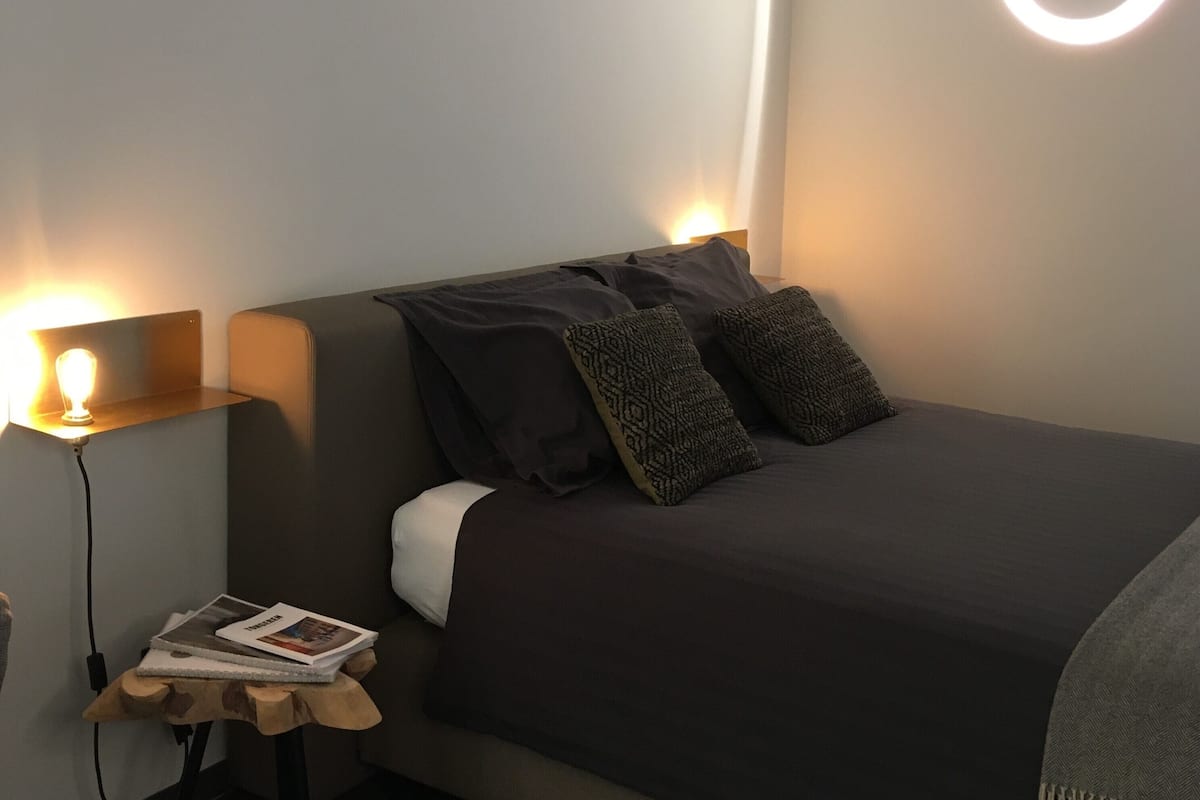 A modern bedroom with a bed, two bedside tables, a nightstand, and a wall-mounted light fixture.