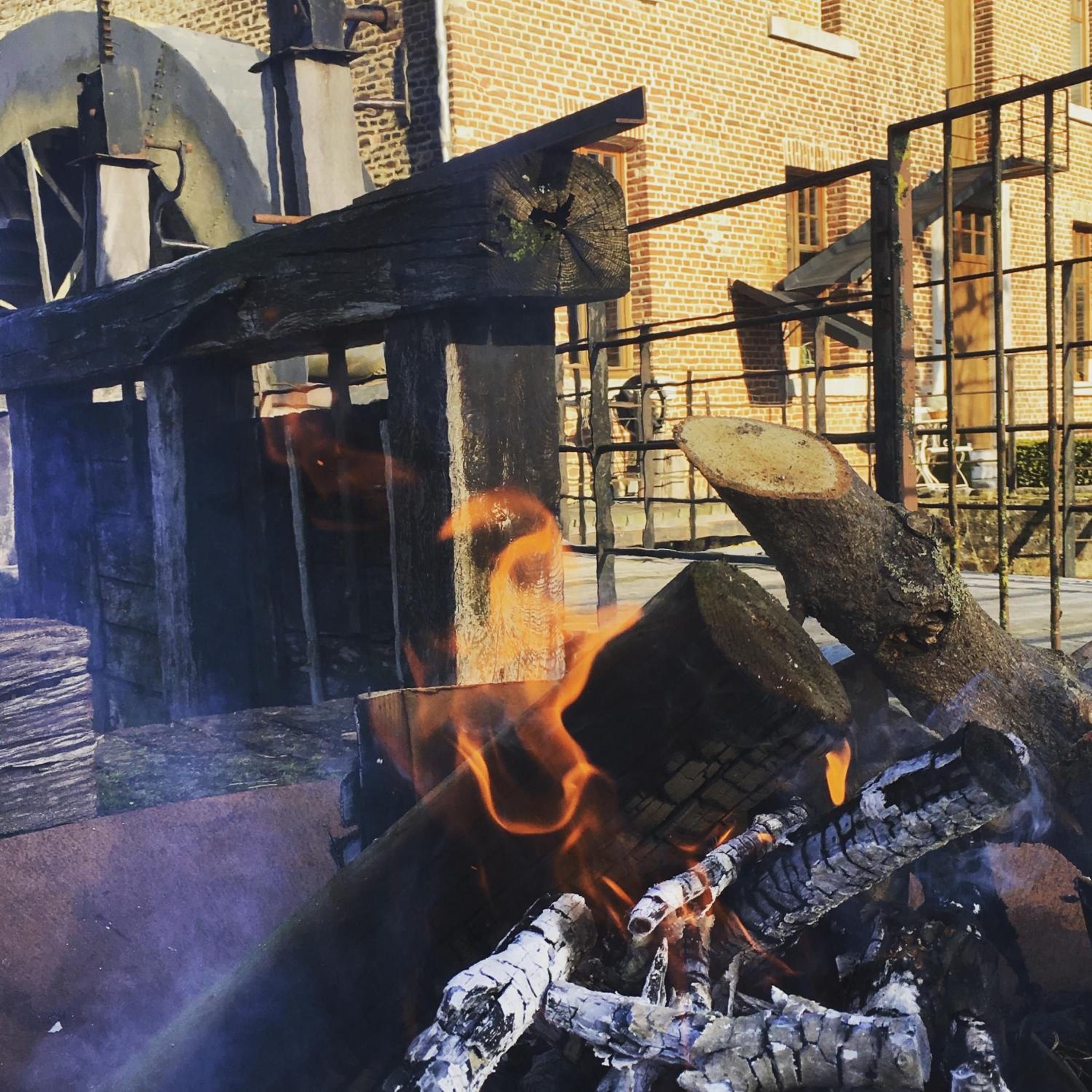 A fire burning in a metal container with a brick wall and a metal gate in the background.