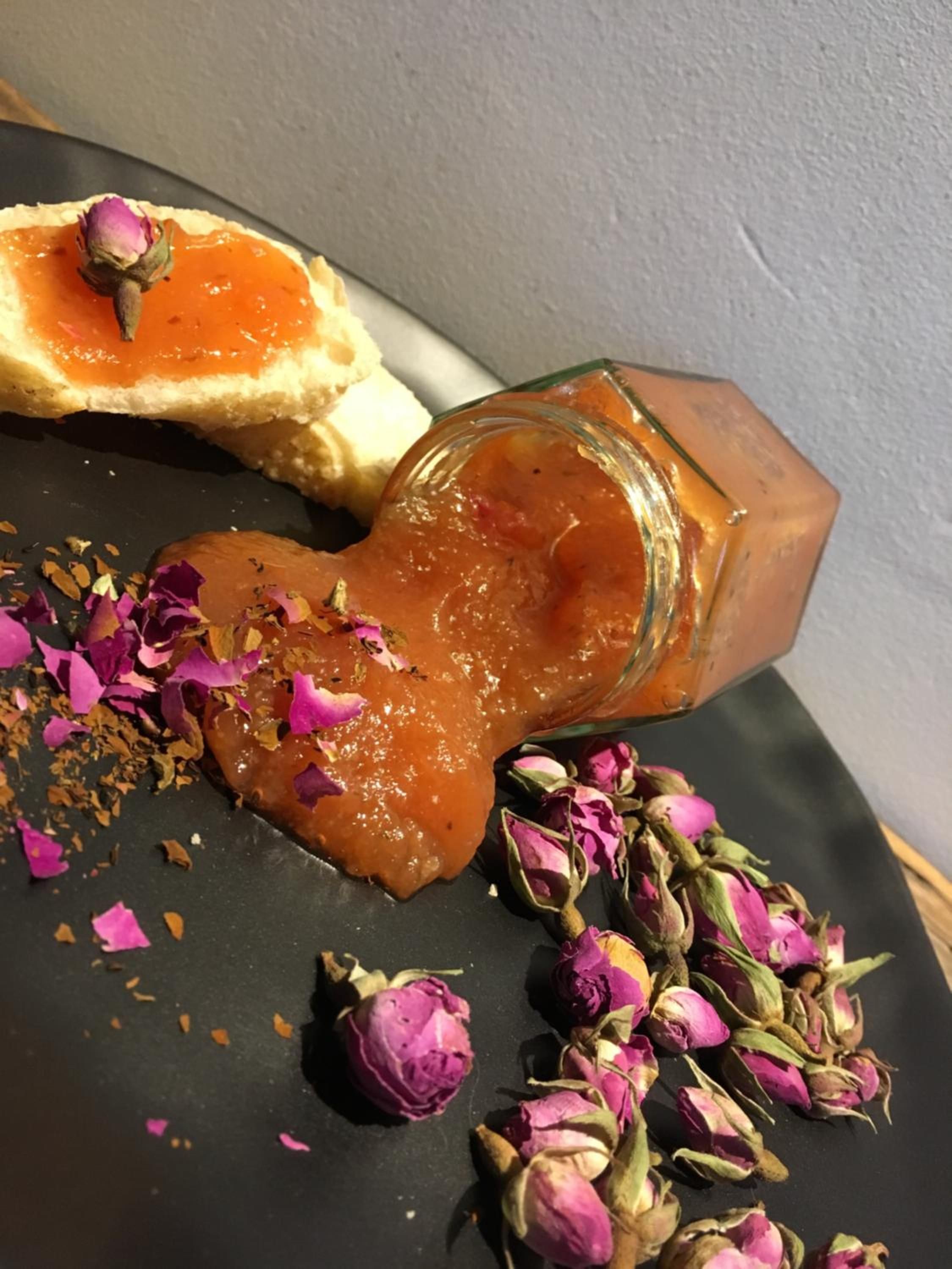 Una ampolla de vidre amb superfície rugosa, una rebanada de pa amb melmelada i flors seques disperses sobre una superfície fosca.