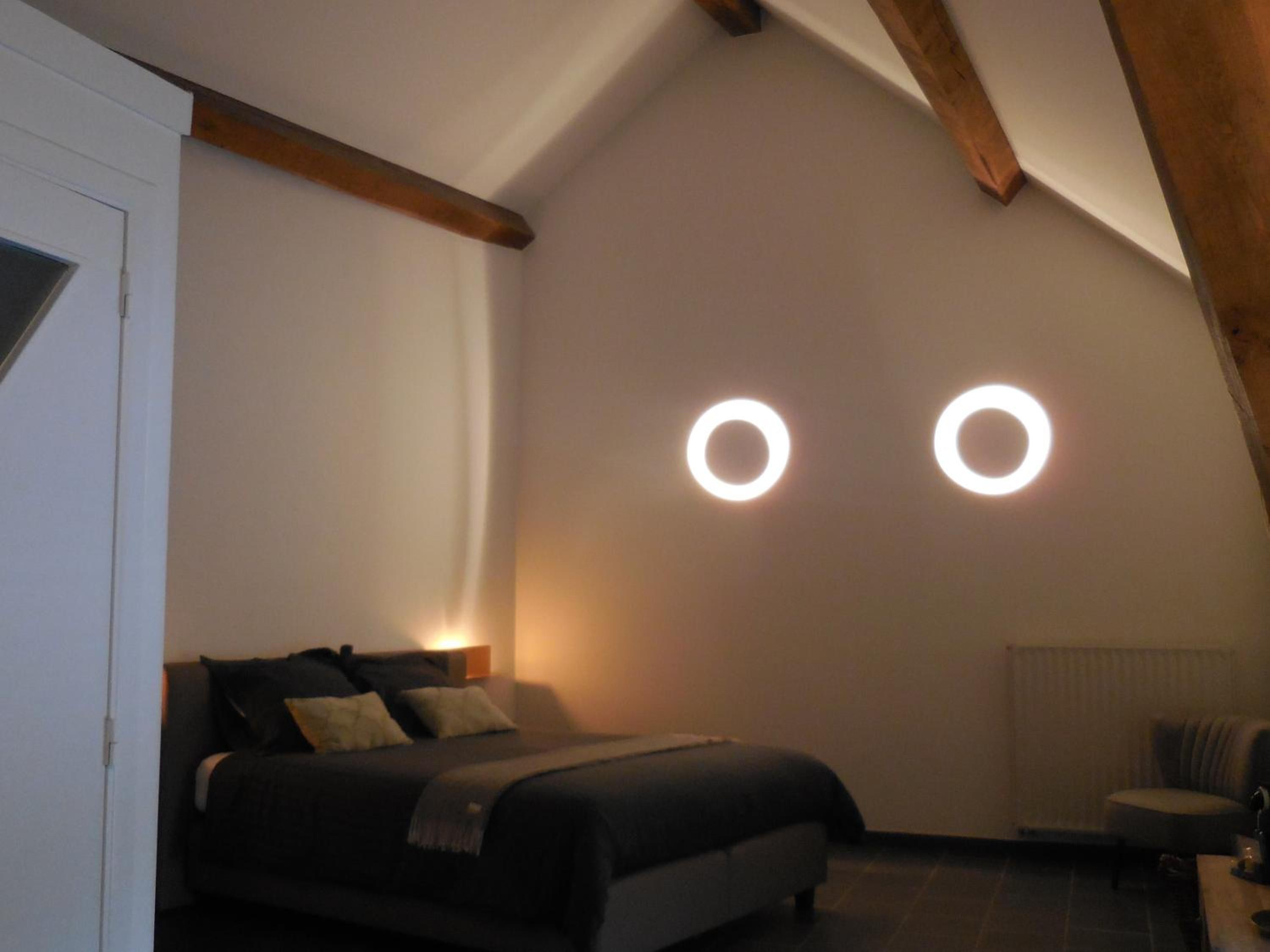 A bedroom with a bed, a chair, and two circular light fixtures on the wall.