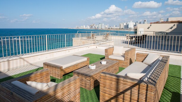 An outdoor seating area with wooden furniture and a view of the ocean and city skyline.