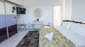 A hotel room with a bed, a TV, a desk, a chair, a mirror, and a door.