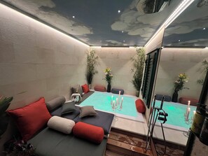 Een gezellig binnenzwembad met een zithoek, een bubbelbad en een plafond met een wolkenmotief.