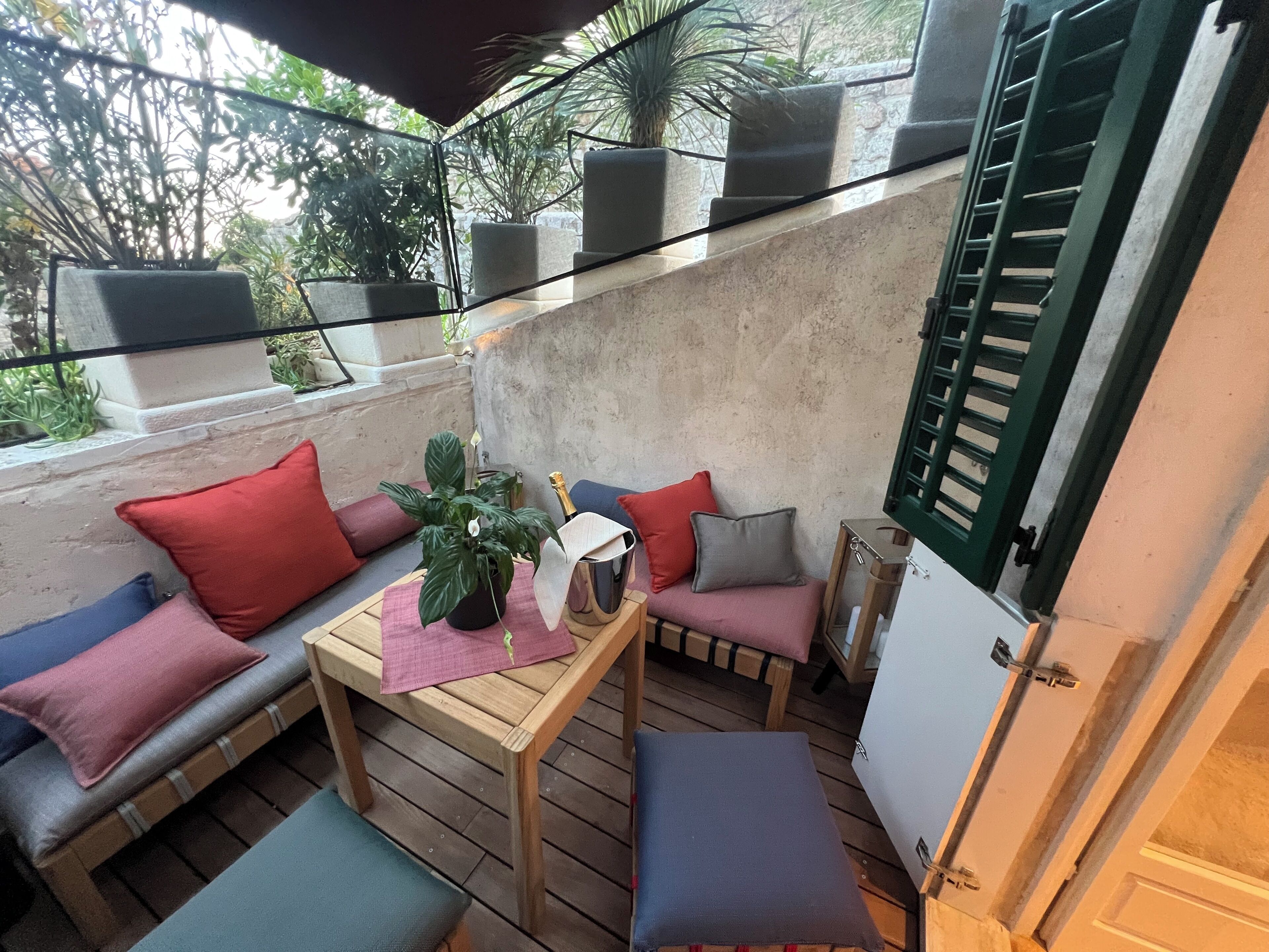 Un espacio al aire libre acogedor con una mesa de madera, asientos acolchados y plantas en macetas.