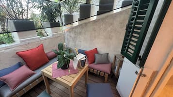 Un espacio al aire libre acogedor con una mesa de madera, asientos acolchados y plantas en macetas.