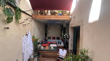 A cozy outdoor seating area with a wooden bench, cushions, and a small table with bottles.