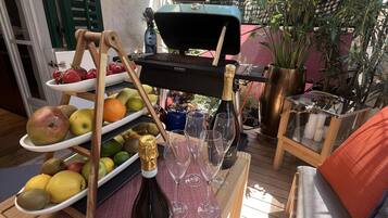 A wooden deck with a grill, fruit platter, wine glasses, and a bottle of Prosecco.